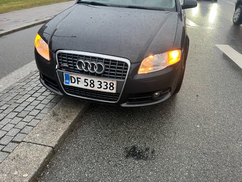 Sort Audi bil parkeret delvist på en kantsten ved våd vej, med forlygter og blinklys tændt. (3)