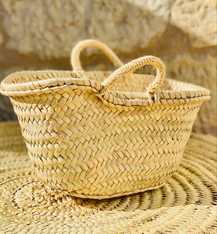 Håndflettet kurv af lyst siv placeret på en flettet måtte med stenbaggrund. (2)