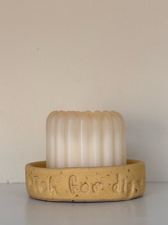 Et hvidt, ribbet stearinlys placeret i en rund beige lerholder med teksten "Jeg for dig" indgraveret.