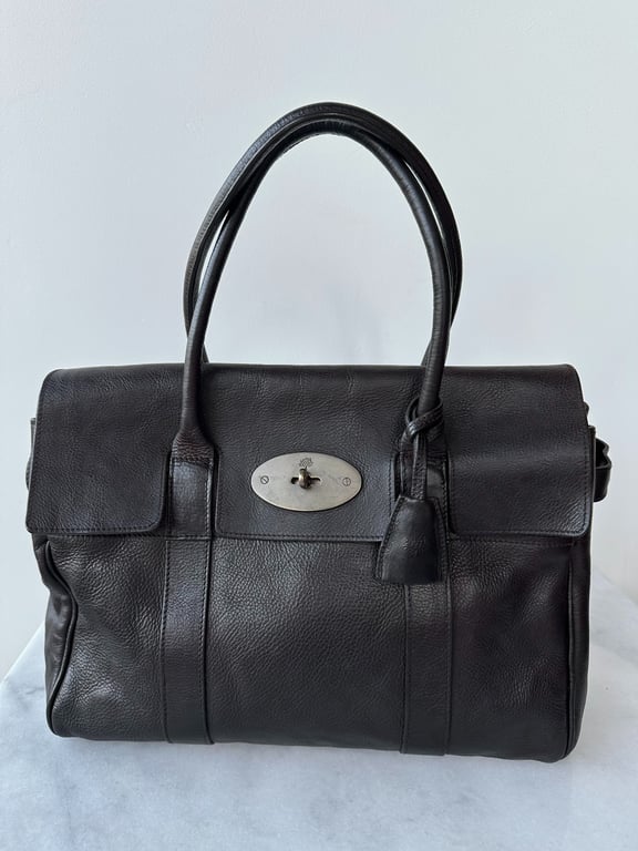 Sort læderhåndtaske med sølvfarvet lås og dobbelte håndtag på neutral baggrund.