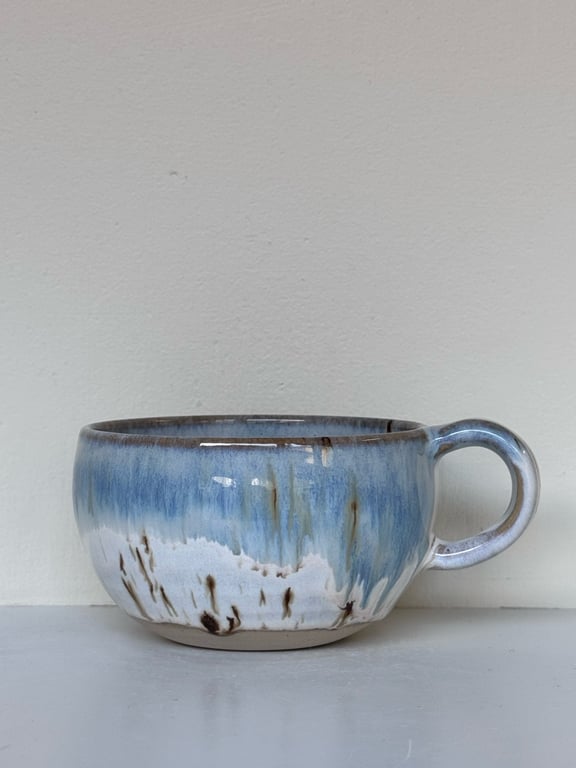 Blå og hvid glasurkrus med hank på grå overflade foran hvid væg.