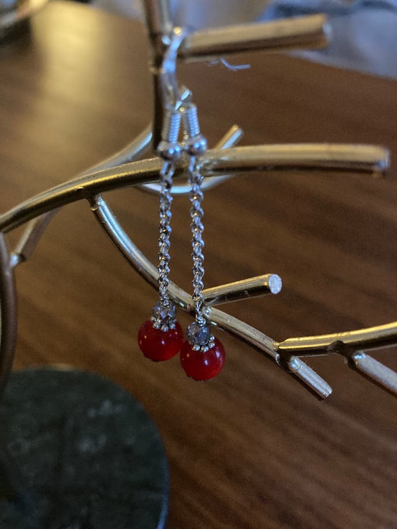 To røde perleøreringe med sølvkæde hængende på en guldfarvet smykkestativ. (2)