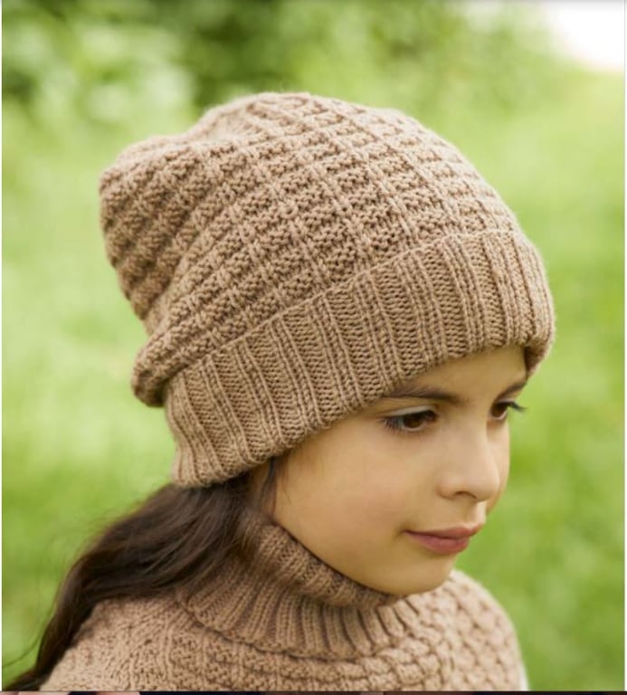 Pige iført beige strikket hue og sweater med grøn baggrund.