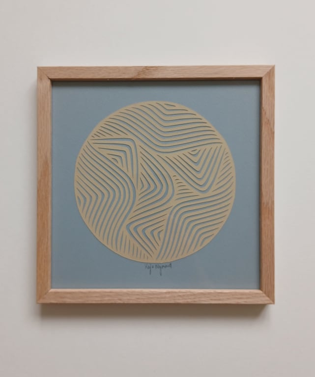 Abstrakt kunstværk med cirkel fyldt med beige, bølgende, linjemønstre på blå baggrund, indrammet i lyst træ.