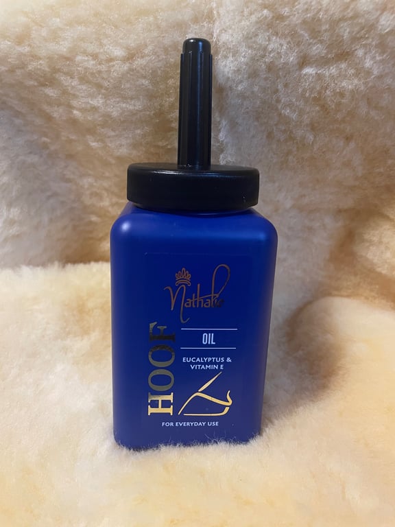 Blå flaske med sort låg mærket "Nathalie Hoof Oil" med eucalyptus og vitamin E, placeret på en blød, cremefarvet overflade.