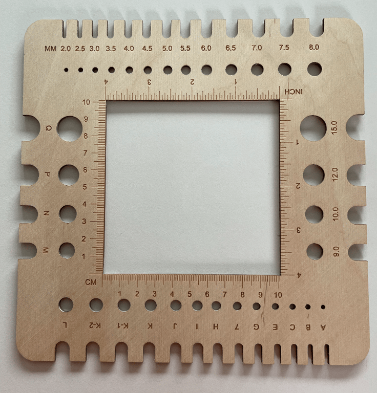 Træværktøj med forskellige måleenheder, huller og indhak til måling og tilpasning af garn, med centimetermål, tommermål og millimeterangivelser.