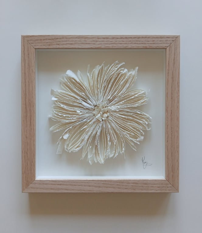 Indrammet hvid blomst lavet af foldede papirblade på hvid baggrund.