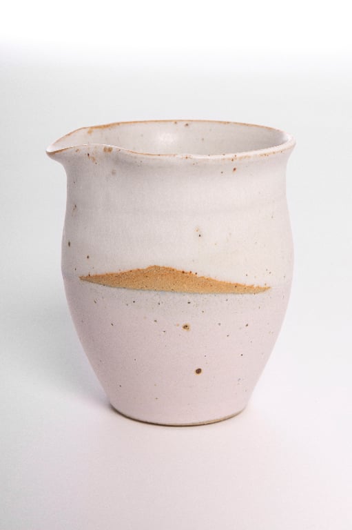 Lille keramisk kande med hvid og beige glasur og let rustfarvet plet på siden.