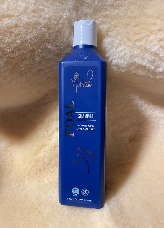 Flaske med blå shampoo uden parfume til heste, mærket "FOAL SHAMPOO" fra Nathalie, stående på lyse uld- eller fåreskindstekstur.