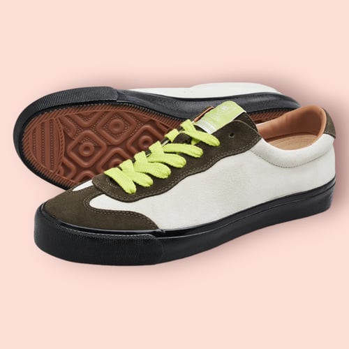 Billede af et par sneakers med hvid og mørkegrøn ruskindsoverdel, sorte såler og lysegrønne snørebånd, placeret på en lyserød baggrund. (2)
