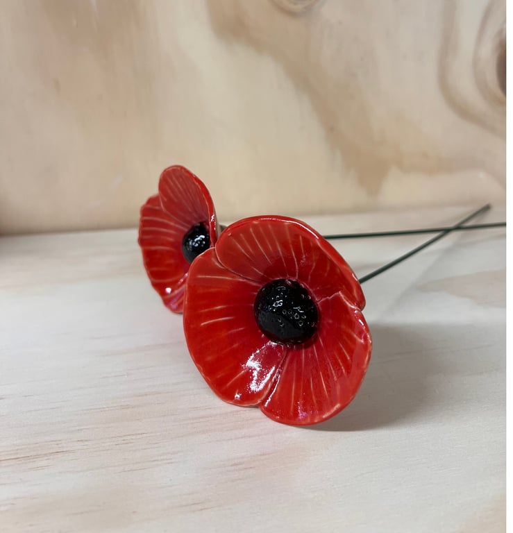 To keramiske valmuer med røde kronblade og sorte centre, lagt på en lys træflade.