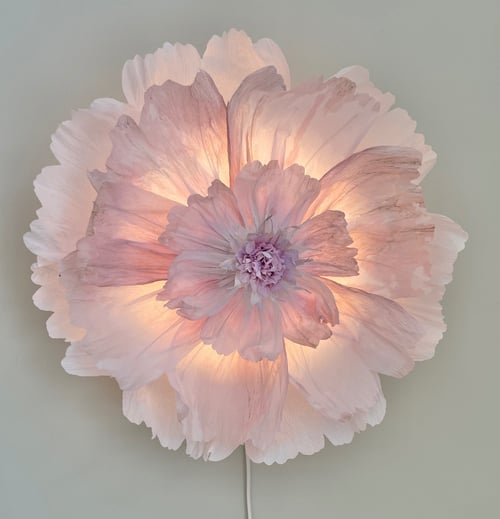 Blomstformet lampe med bløde lyserøde blomsterblade oplyst indefra på en grå væg. (1)