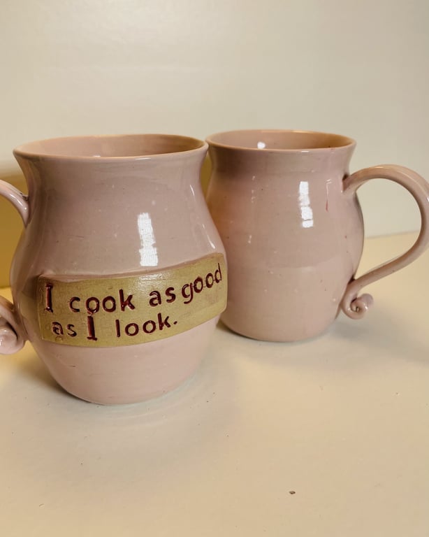 To rosa keramikkrus, hvor det ene har teksten "I cook as good as I look." skrevet på en gul baggrund.
