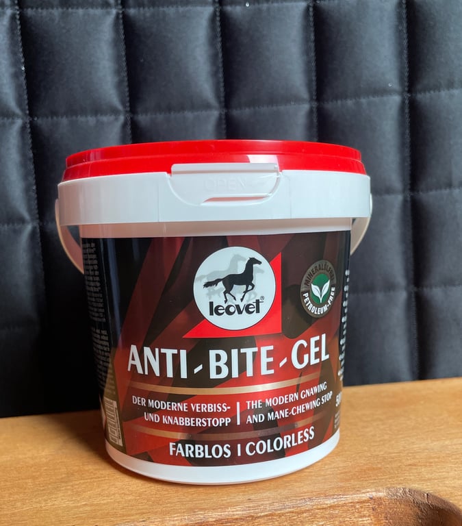 Bøtte med Leovet Anti-Bite Gel, en farveløs gel mod tygning og bidning til heste, placeret på et træbord med en quiltet sort baggrund.