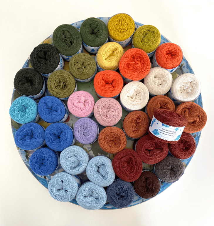 Rundt fad med flere nøgler garn i forskellige farver, herunder grønne, gule, orange, røde, blå, lilla og brune nuancer, på hvid baggrund.