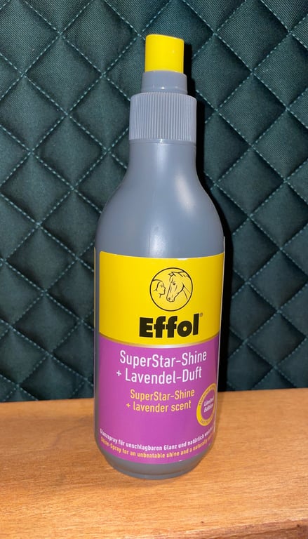 Grå plastikflaske med gul sprayhætte og gul-lilla etikette med teksten "Effol SuperStar-Shine + Lavendel-Duft" stående på et træbord foran en quiltet mørkegrøn baggrund.