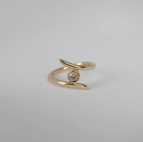 Guldring med åbenende design og en enkelt rund diamant i midten, placeret på hvid baggrund. (1)