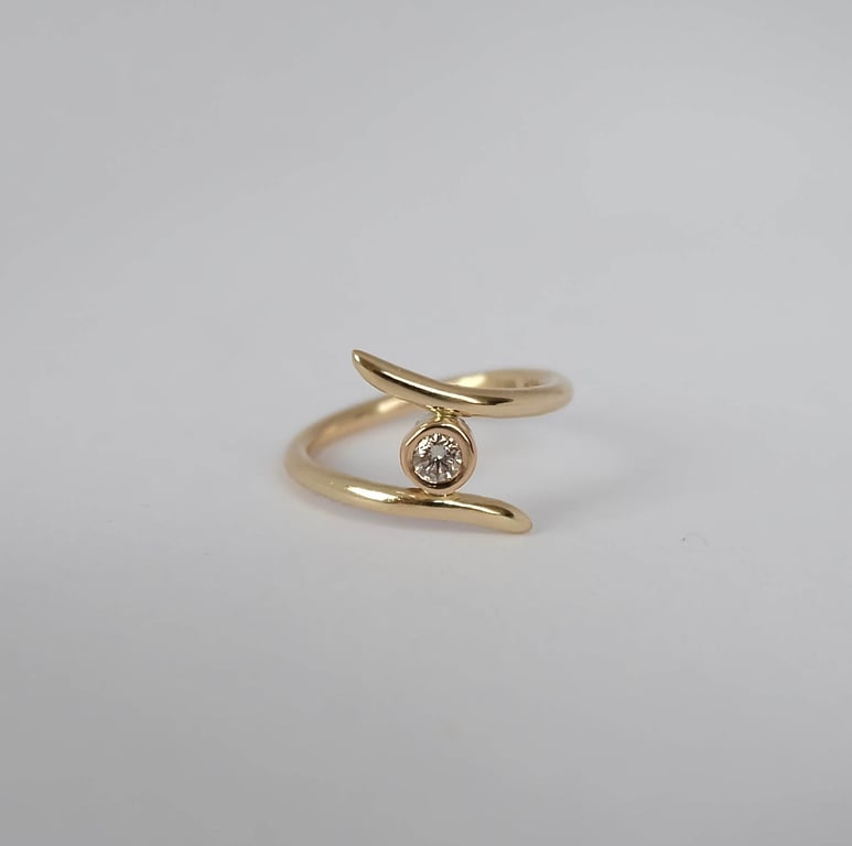 Guldring med åbenende design og en enkelt rund diamant i midten, placeret på hvid baggrund.