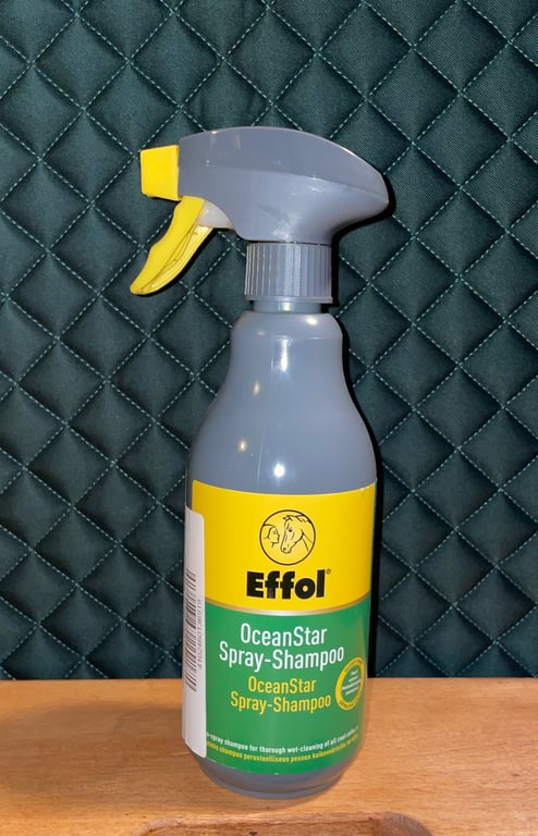 Sprayflaske med Effol OceanStar Spray-Shampoo til heste, placeret på et bord foran en sort quiltet baggrund.