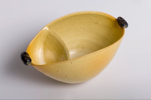 Gul oval keramisk skål med en skillevæg i midten og to små mørke håndtag i hver ende.