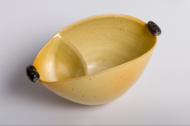 Gul oval keramisk skål med en skillevæg i midten og to små mørke håndtag i hver ende.