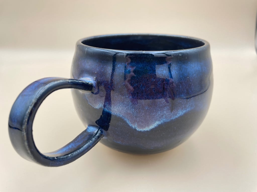 Blå keramisk kop med skinnende glasur på lys baggrund.