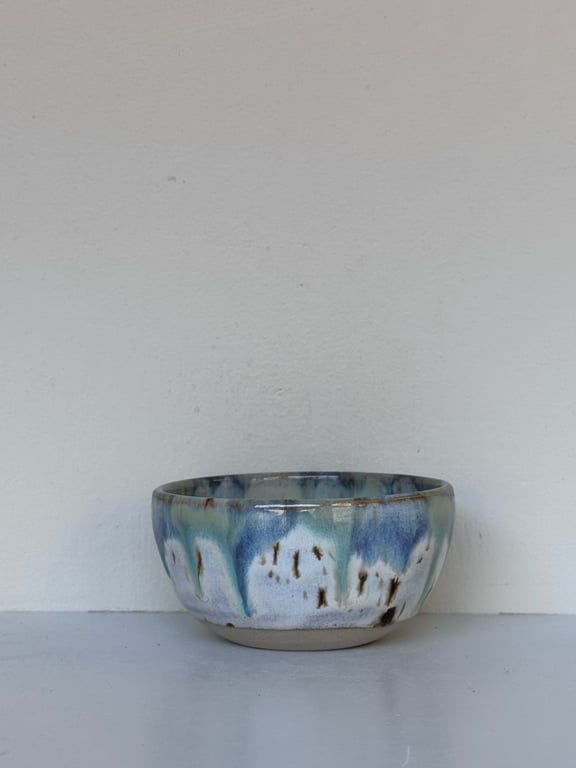 Keramikskål med abstrakt blå, grøn og brun glasur mod en lys baggrund.