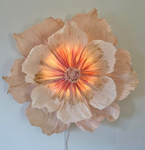 Stor væglampe formet som en blomst med rosa og hvide nuancer, der lyser varmt indefra. (1)