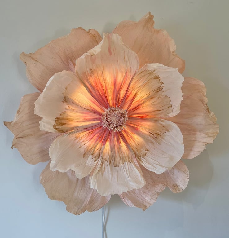 Stor væglampe formet som en blomst med rosa og hvide nuancer, der lyser varmt indefra.