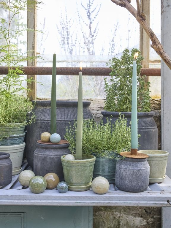 Billede af grønne planter i potter og tændte grønne stearinlys placeret på en vindueskarm med keramiske kugler rundt omkring.