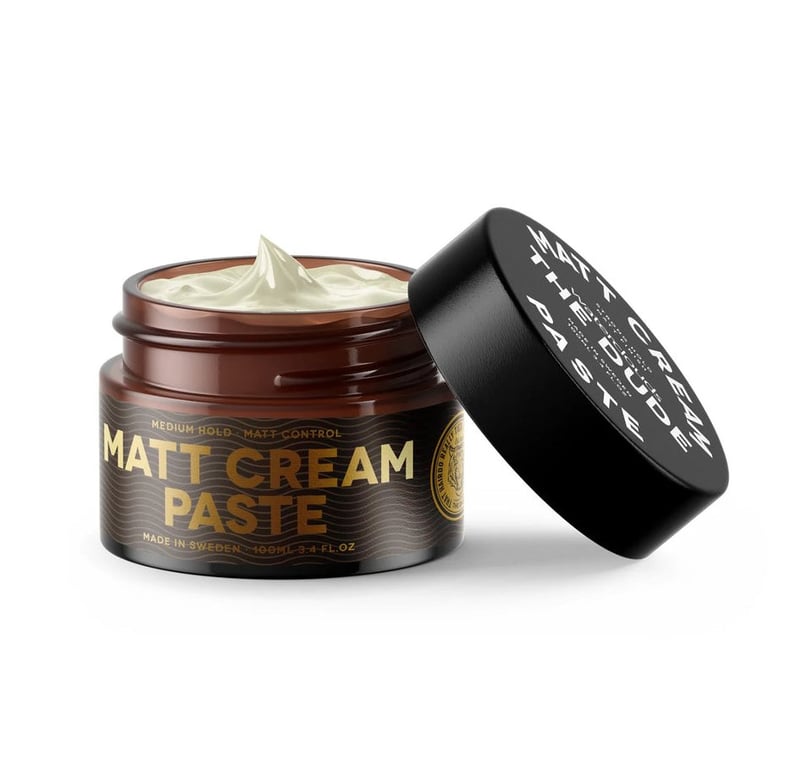 Åben beholder med Matt Cream Paste hårstylingprodukt i brun glasbeholder med sort låg, cremefarvet pasta synlig.