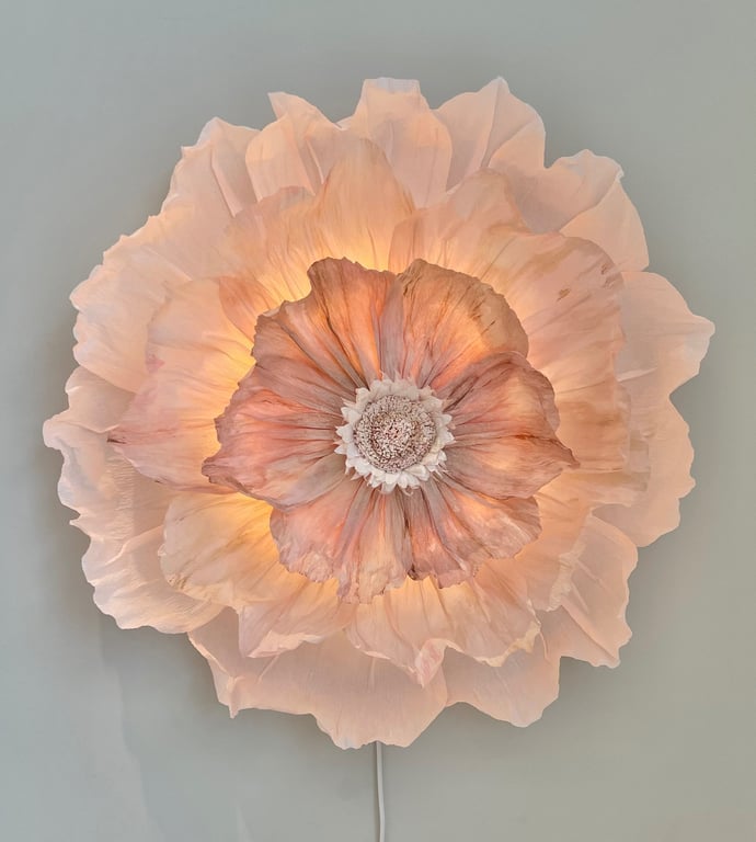 Blomst formet væglampe med bløde, rynkede kronblade i lyserøde og peach nuancer, der udsender varmt lys.