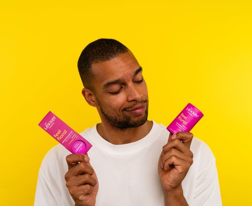 Mand i hvid t-shirt holder to pink produkter med teksten "feel floral" på en gul baggrund. (1)