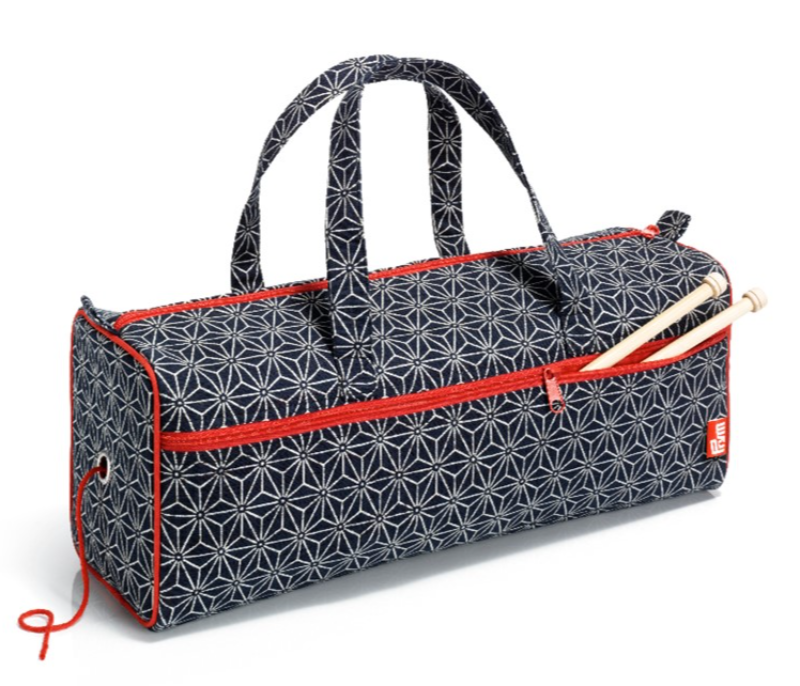 Strikketaske med blå og hvide mønstre, rød lynlås og to strikkepinde i et yderrum.