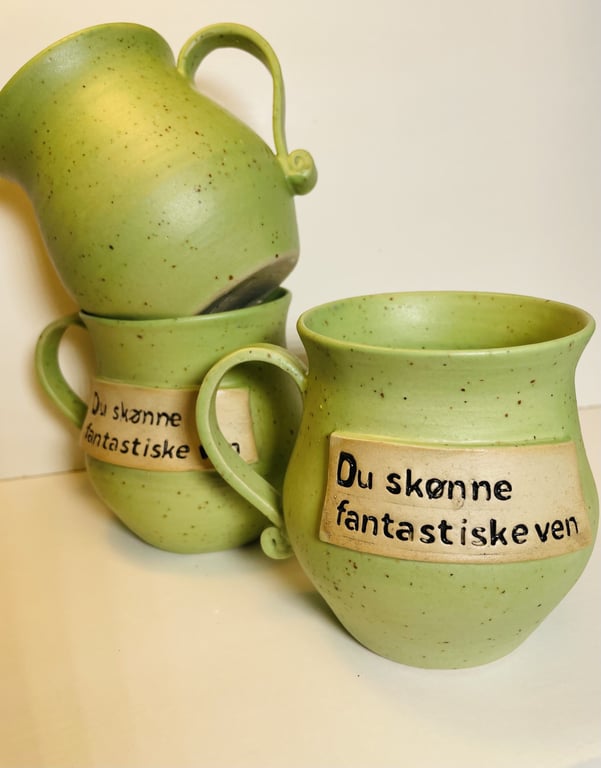 Tre grønne keramikkrus med hank, hvorpå der står skrevet "Du skønne fantastiske ven".