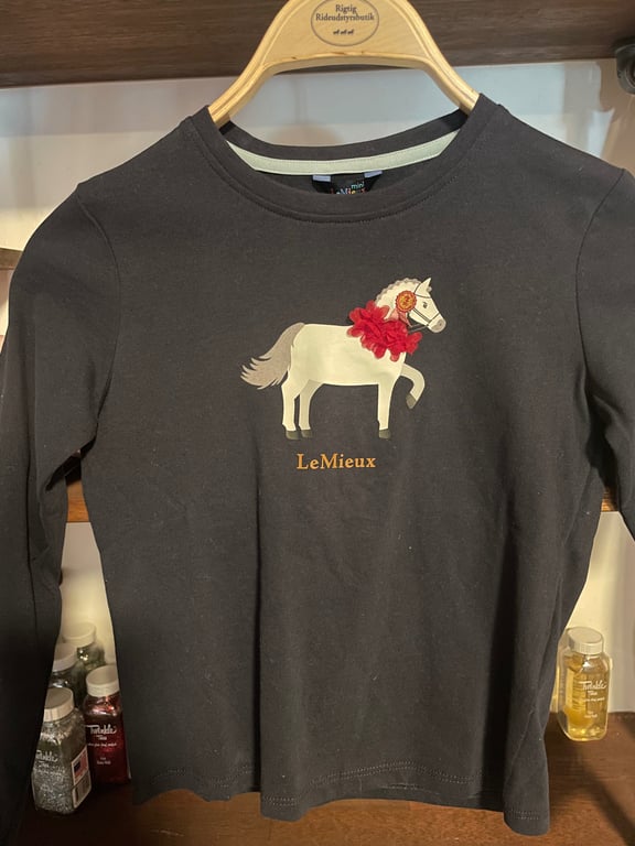 Langærmet sort t-shirt med motiv af en hvid hest pyntet med en rød blomst og teksten "LeMieux" foran.