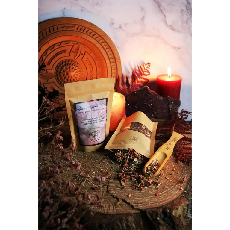 To pakker med tørret urteblanding, en træske med tørrede urter, et stearinlys, lyserød sten og en rund træplade med udskæringer, sat op på et rustikt træstykke med tørrede planter omkring. (2)