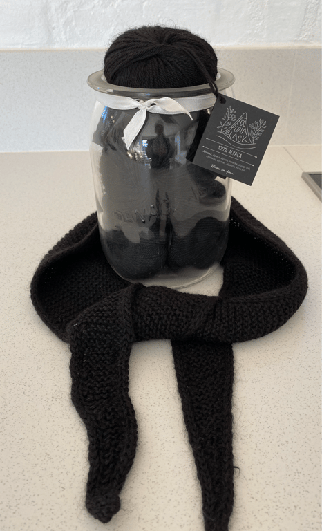 Sort garn i en glasbeholder med et sort strikket tørklæde lagt rundt om beholderens bund.