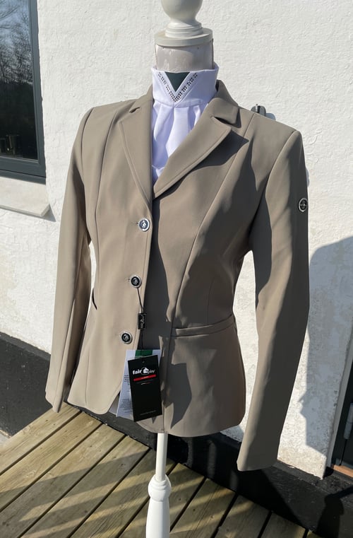 Beige ridingjakke på mannequin med hvid skjorte under, fotograferet udendørs foran hvid væg. (1)