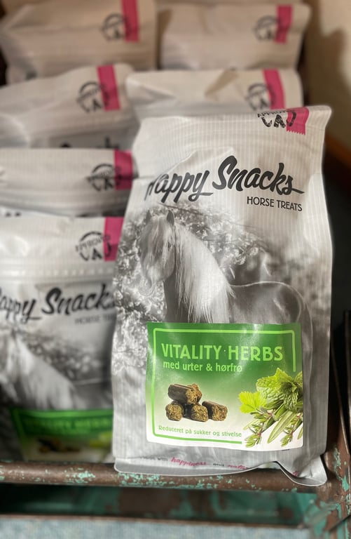 Pakker med Happy Snacks hestegodbidder, Vitality Herbs med urter og hørfrø, vist på en hylde.