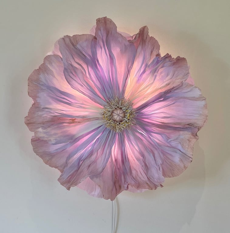 Stor, lysende lampe formet som en detaljeret pink og lilla blomst, der hænger på en væg.