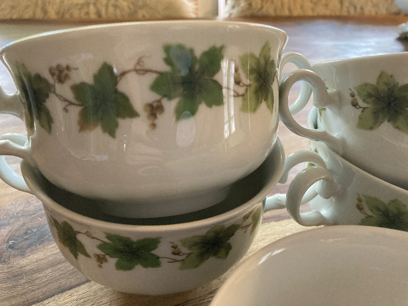 Stak af hvide porcelænsskåle med grønne blade og små bær som dekoration, placeret på et træbord. (2)