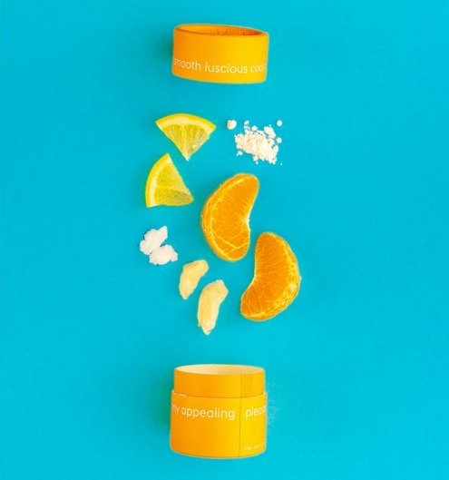 Orange kosmetikbeholder med citrusfrugtskiver og pulver på en blå baggrund. (1)