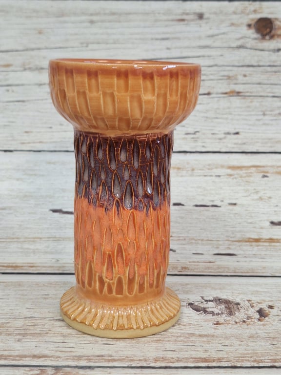 Keramisk vase med tekstureret overflade i brune og orange nuancer, stående på træbord.