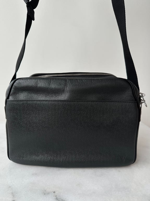 Sort skuldertaske i læder med tekstur og justerbar rem, placeret på en marmorbordplade.