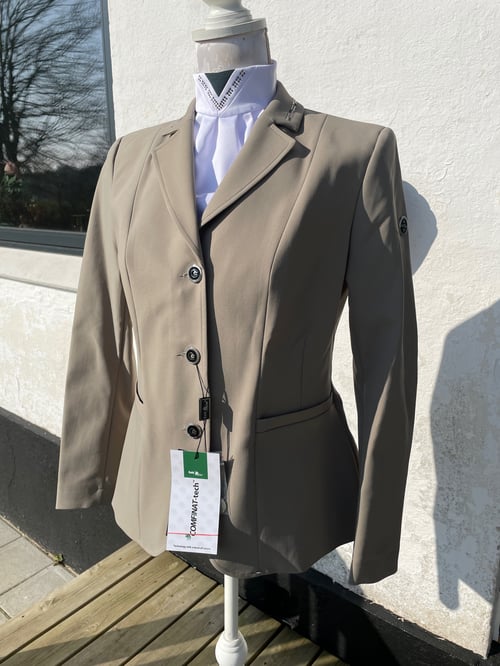 Beige ridejakke med knapper og tag, vist på mannequin uden hoved mod en hvid væg i sollys. (1)