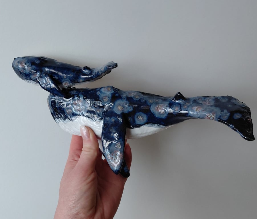Hånd, der holder en blå og hvid keramikfigur af en hval med blomsterlignende mønstre.