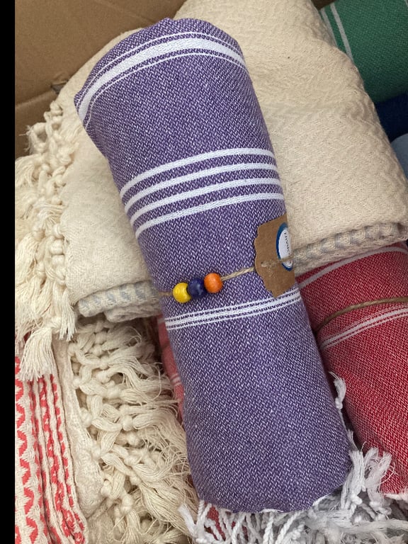 Rullede og foldede vævede bomuldstekstiler i forskellige farver, herunder lilla, rød og beige, med frynser og små træperler som pynt. (2)