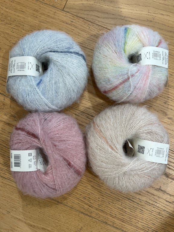 Fire nøgler blødt mohairgarn i forskellige farver, placeret på et lyst træbord.