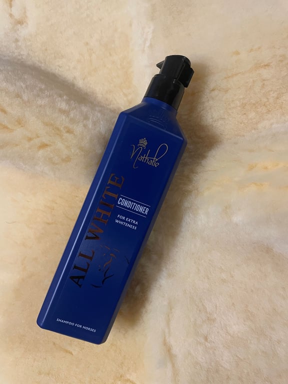 Blå flaske med balsam mærket "Nathalie All White Conditioner" til heste, lagt på en blød, beige overflade.